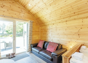 A wooden interior with a leather sofa, a bench, and a door leading outside. - Comfortable pod perfect for short stays for couples with a sense of fun. (Hawes,)