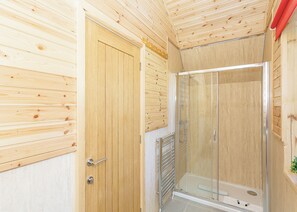 A wooden-paneled room with a glass-enclosed shower and a door. - Comfortable pod perfect for short stays for couples with a sense of fun. (Hawes,)