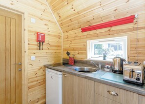 A compact kitchen with wooden walls, a stainless steel sink, a toaster, and a window with a view of the outside. - Comfortable pod perfect for short stays for couples with a sense of fun. (Hawes,)