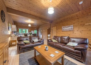 Ein Holzblockhaus-Interieur mit zwei Ledersofas, einem Holztisch und einem durch eine offene Tür einsehbaren Küchenbereich.