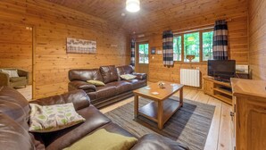 En stuga med träpanel på insidan, inredd med en soffa, ett soffbord, en tv och ett fönster med gardiner.