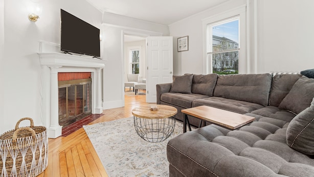 A living room with a fireplace, a large sofa, a coffee table, and a television mounted on the wall.