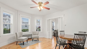 A dining area with a wooden table and black chairs, a ceiling fan, and large windows with blinds.