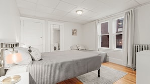 A bedroom with a bed, bedside table, lamp, and a window with blinds.