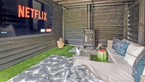 Ein gemütliches Zimmer mit Netflix-Bildschirm, Kaminofen, einem Bett mit gemusterten Betttextilien und einem kleinen Tisch mit Wassermelone.