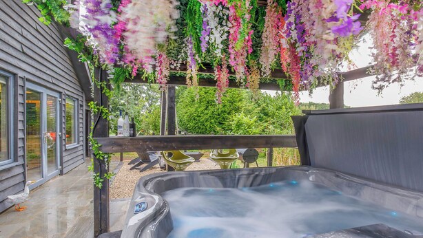 A hot tub with a wooden deck, surrounded by hanging flowers, and a view of a house in the background. - 1 bedroom accommodation in South Duffield, Nr York (South Duffield, Nr York)
