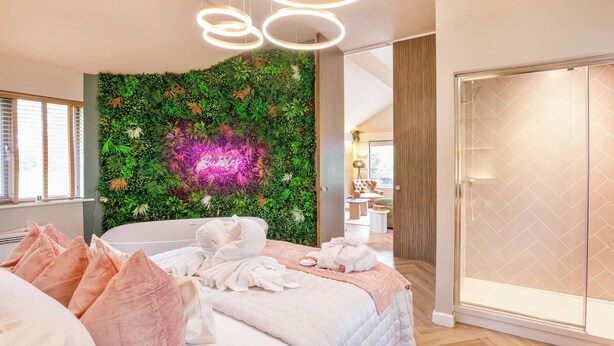 Ein modernes Schlafzimmer mit einem Bett, einer grünen Wand mit einer Neonreklame, einem Glastisch und einer runden Leuchte.