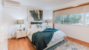 Une chambre à coucher avec un lit, des lampes de chevet, une fenêtre donnant sur des arbres et un tableau accroché au mur.