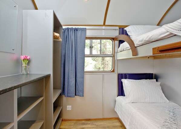 Uma cabana compacta com cama beliche, uma mesa pequena e uma janela com cortinas.