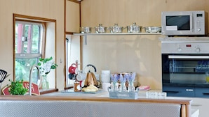 A kitchen with a microwave, oven, and a window with a view of trees. - Brunel Boutique Railway Carriage 1 (Dawlish Warren)
