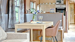 A dining area with a table, chairs, a vase with flowers, and a wine glass. - Brunel Boutique Railway Carriage 1 (Dawlish Warren)