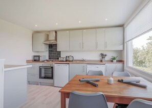 A modern kitchen with white cabinets, a wooden countertop, a built-in oven, and a dining area with a table and chairs. - 1 bedroom accommodation in South Molton, nr Barnstaple (South Molton, nr Barnstaple)