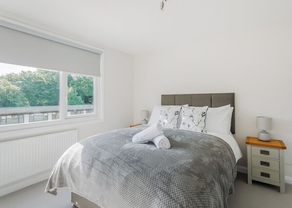Une chambre avec un grand lit, une fenêtre donnant sur un beau paysage, une table de chevet avec une lampe et un radiateur.