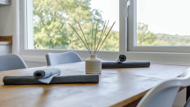A wooden table with a white vase and reed diffuser, a rolled-up mat, and a chair. - 2 bedroom accommodation in South Molton, nr Barnstaple (South Molton, nr Barnstaple)