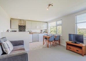 A modern kitchen with white cabinets, a dining area with a wooden table and chairs, a grey sofa, and a TV on a wooden stand. - 1 bedroom accommodation in South Molton, nr Barnstaple (South Molton, nr Barnstaple)