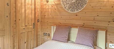 A wooden room with a bed, two pillows, a wall-mounted light fixture, and a decorative plate.