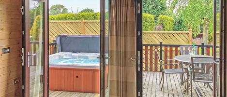 A hot tub on a wooden deck with a glass door leading to a patio area.