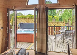 A hot tub on a wooden deck with a glass door leading to a patio area.