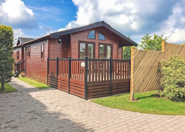 Une maison mobile en bois dotée d’un patio clos, d’un chemin en briques et d’une clôture en bois.