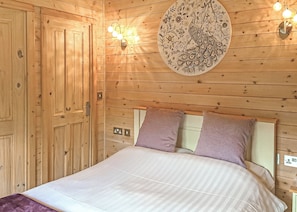 Une pièce en bois avec un lit, deux oreillers, un luminaire fixé au mur et une assiette décorative.