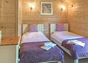 Une chambre avec deux lits, des murs en bois et deux lampes fixées au mur.