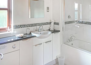 Une salle de bain avec un lavabo blanc, un miroir, une cabine de douche en verre et un pare-splash en carrelage.