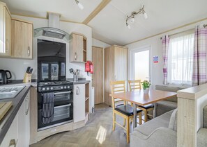 Une cuisine compacte équipée d’une cuisinière, d’un four et d’une machine à café. On y trouve également un coin repas avec une table et des chaises, ainsi qu’un canapé.