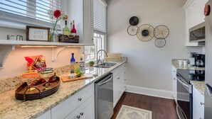 A modern kitchen with white cabinetry, a granite countertop, and a built-in dishwasher. There are decorative wall art pieces and a window with blinds. - Stovall #3 Historic & walkable to downtown Augusta hotspots (Augusta)