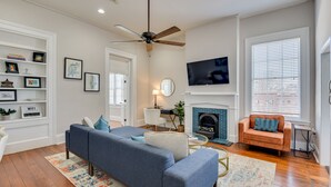 A living room with a blue sofa, a fireplace, a television, and a ceiling fan. - Stovall #3 Historic & walkable to downtown Augusta hotspots (Augusta)