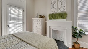 A bedroom with a bed, dresser, fireplace, and decorative wall panels. - Stovall #3 Historic & walkable to downtown Augusta hotspots (Augusta)