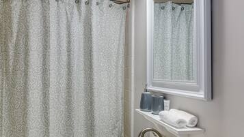 A bathroom with a shower curtain, a sink, a mirror, and a wall-mounted light fixture.