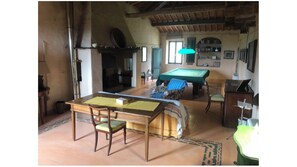 Um quarto com mesa de bilhar, mesa de jantar com cadeiras, sofá e piano.
