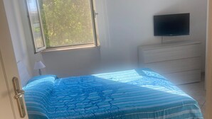 Une chambre à coucher avec un lit, un téléviseur posé sur une commode et une fenêtre donnant sur des arbres.