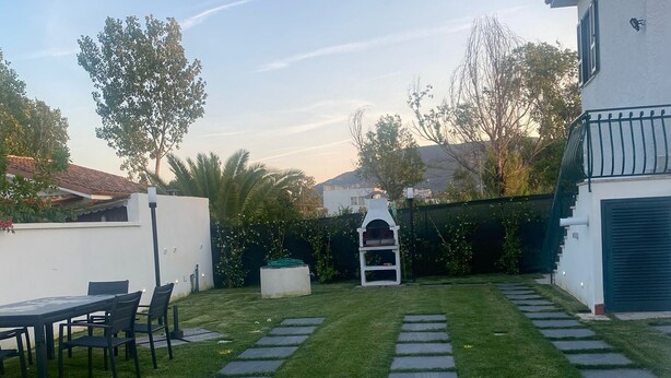 Un jardin bien entretenu avec une pelouse, un chemin de pierres et un espace repas équipé de chaises.