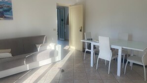 Un salon moderne avec un canapé blanc, une table à manger en verre entourée de chaises et un tableau accroché au mur.