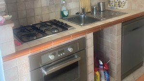 Une cuisine équipée d’une cuisinière à gaz, d’un four, d’un évier en acier inoxydable et de meubles de rangement en bois.
