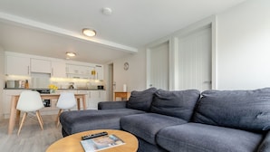 Ein modernes Wohnzimmer mit grauem Sofa, einem Holztisch und einer Küche im Hintergrund.