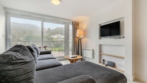 Ein modernes Hotelzimmer mit einer großen Couch, einem an der Wand befestigten Fernseher und Blick ins Freie.