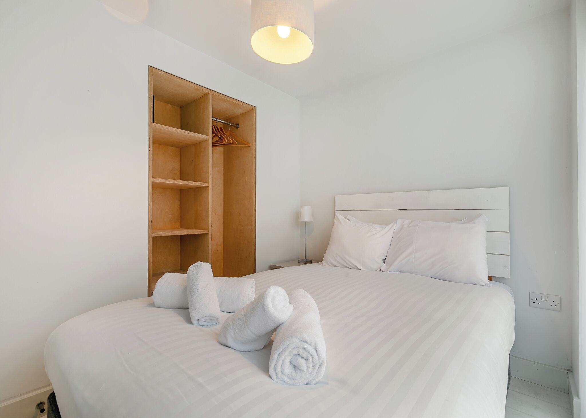 A hotel room with a bed, a wooden wardrobe, and a bedside lamp.