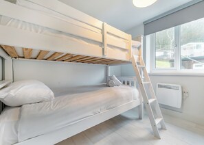 A bunk bed with a wooden ladder, a white radiator, and a window with a view of houses. - Sea Shore apartments are perfect for families. (Millendreath, Looe)