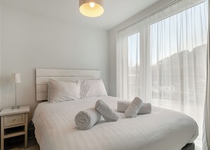 A hotel room with a bed, a nightstand, a lamp, and sheer curtains.