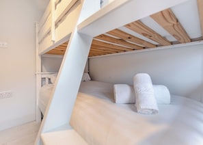 Un lit superposé avec une literie blanche et deux serviettes enroulées.