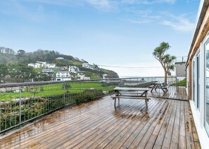 A wooden deck with picnic tables, a view of the sea, and houses in the background.