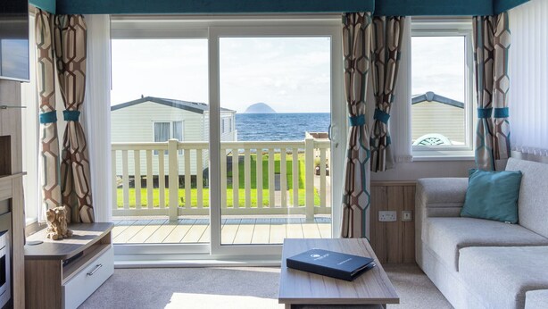 Una habitación con sofá, mesa, televisor y vistas al mar a través de amplias ventanas.