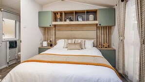 Ein Schlafzimmer mit einem Bett, einem Kopfteil, einer Ablage mit Dekoration, einem Nachttisch und einem Fenster mit Vorhängen.