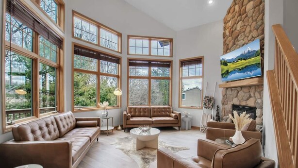 Un amplio salón con ventanas grandes, una chimenea de piedra y una zona de estar acogedora.