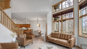 Amplio salón con techo alto, una escalera y ventanas grandes.