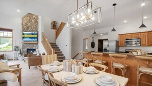Un salón amplio con chimenea, una mesa de comedor dispuesta para una comida y una cocina con armarios de madera y electrodomésticos modernos.
