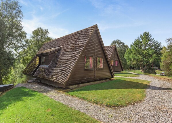 A traditional wooden house with a sloped roof, surrounded by a gravel path and greenery. - Delny Highland Lodge (Delny, Nr Invergordon)