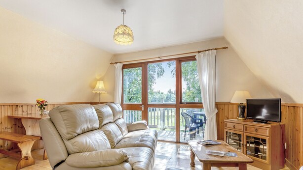 Ein geräumiges Wohnzimmer mit Ledersofa, Fernseher und Couchtisch aus Holz.
